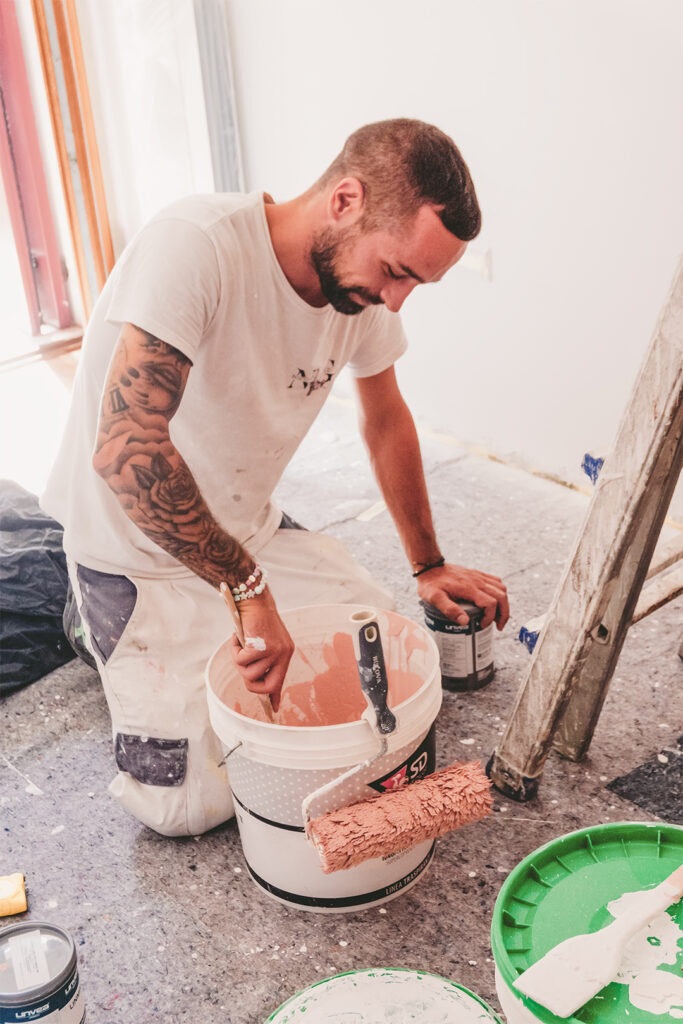 Imbianchino prepara vernice color terracotta nel secchio, con rullo e scala in cantiere; pittura interni NGColor – progetto di Natalia Canaletti
