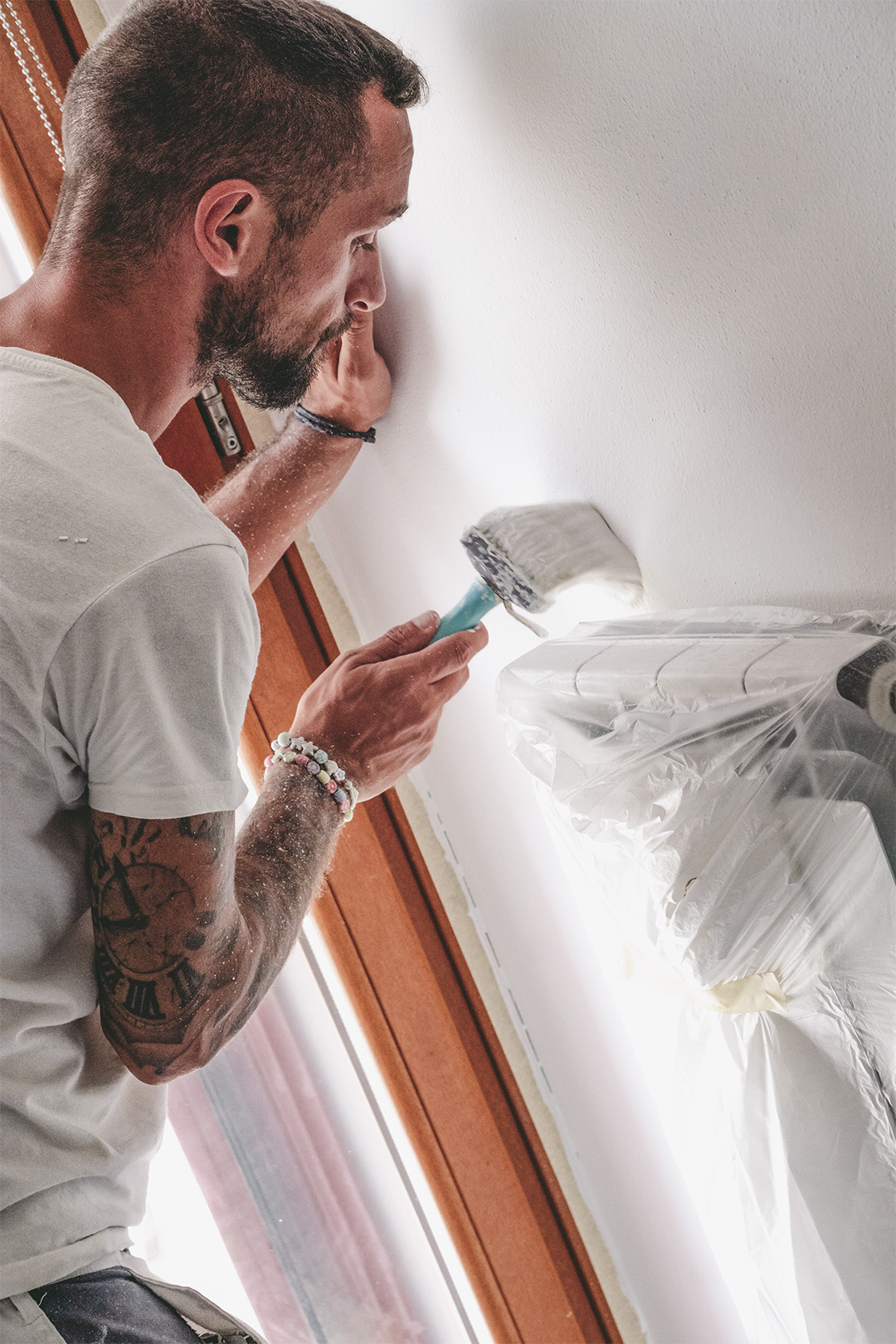 Imbianchino al lavoro mentre dipinge una parete interna con pennello, intervento di pittura d’interni in abitazione
